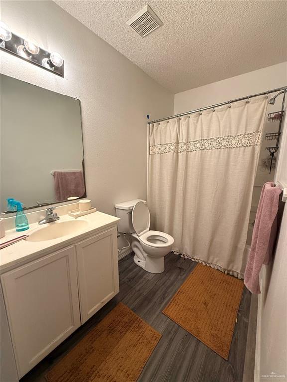 1341 Kokopelli Dr, Edinburg, TX 78541 - bathroom with a textured ceiling, toilet, wood finished floors, vanity, and curtained shower