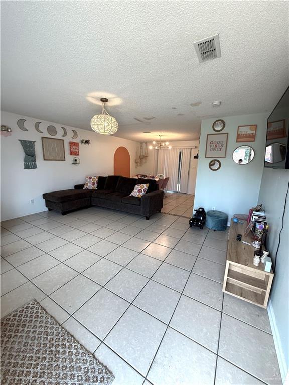1341 Kokopelli Dr, Edinburg, TX 78541 - living room featuring light tile patterned flooring, a textured ceiling, a chandelier, and arched walkways