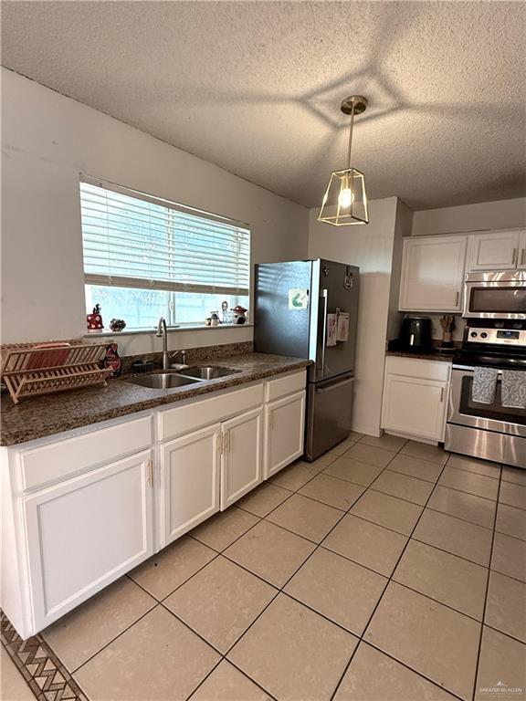 1341 Kokopelli Dr, Edinburg, TX 78541 - kitchen with stainless steel appliances, a sink, dark countertops, a textured ceiling, and light tile patterned floors