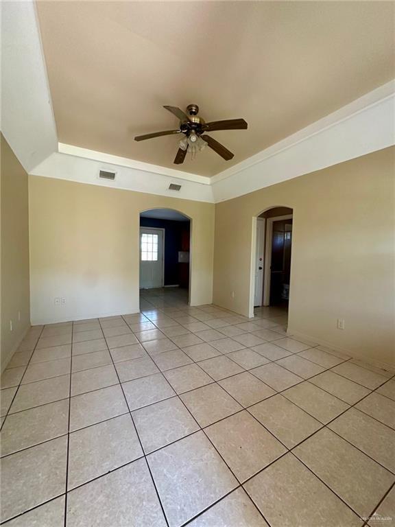 unfurnished room featuring arched walkways, ceiling fan, light tile patterned floors, visible vents, and a raised ceiling