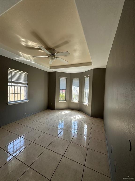 empty room featuring a tray ceiling, light tile patterned flooring, a wealth of natural light, and a ceiling fan