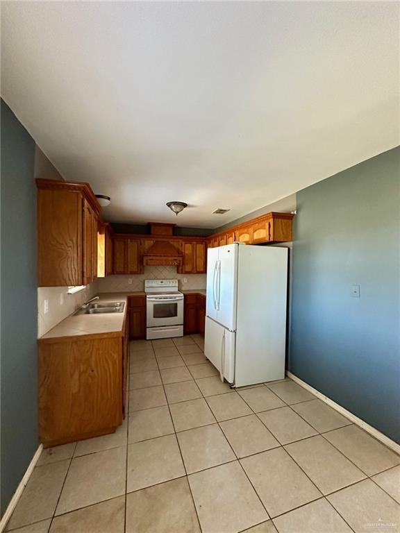 kitchen featuring white appliances, light tile patterned floors, lofted ceiling, light countertops, and a sink