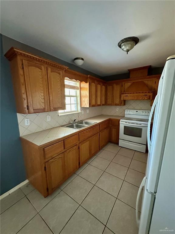 kitchen with white appliances, tasteful backsplash, light tile patterned floors, tile counters, and a sink