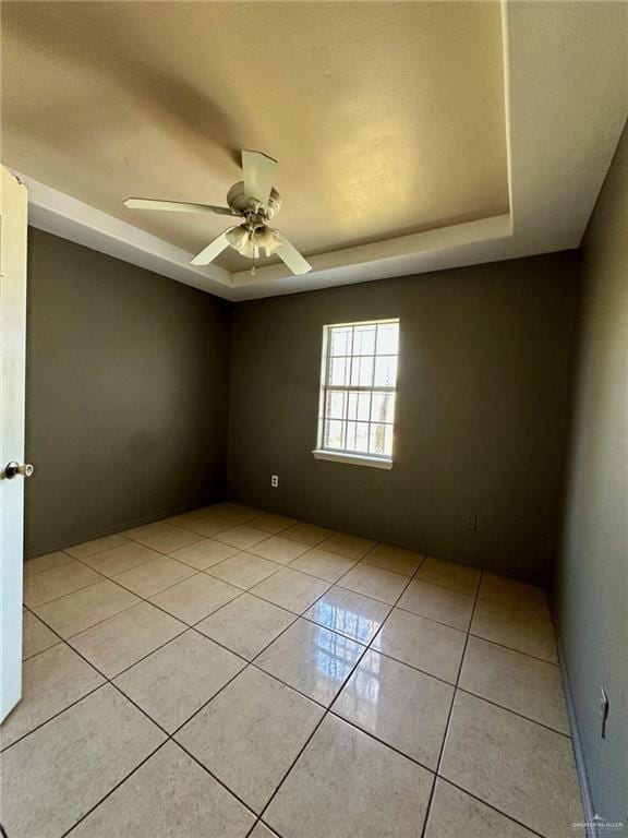 unfurnished room featuring a ceiling fan, a raised ceiling, and light tile patterned floors