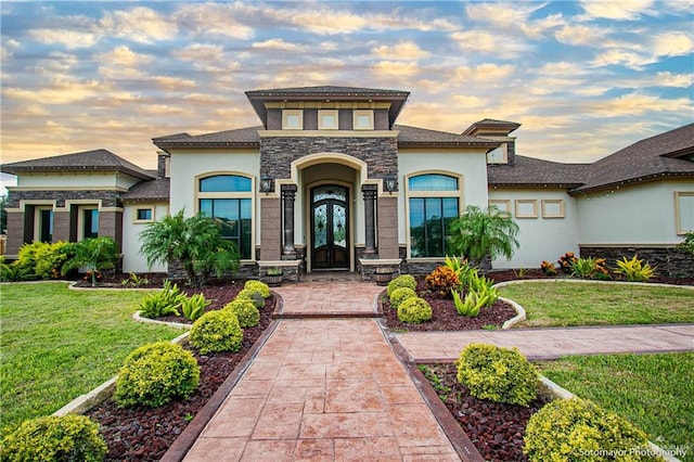 view of front facade featuring a front yard, french doors, stone siding, and stucco siding