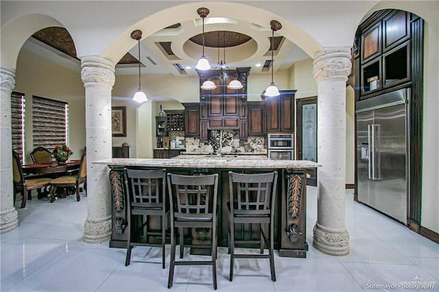 kitchen with dark brown cabinets, a breakfast bar, decorative columns, decorative backsplash, and stainless steel appliances