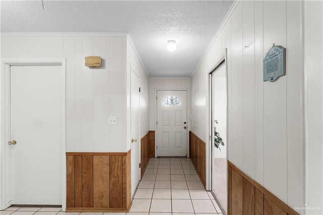 doorway to outside with a textured ceiling, light tile patterned floors, crown molding, and wooden walls