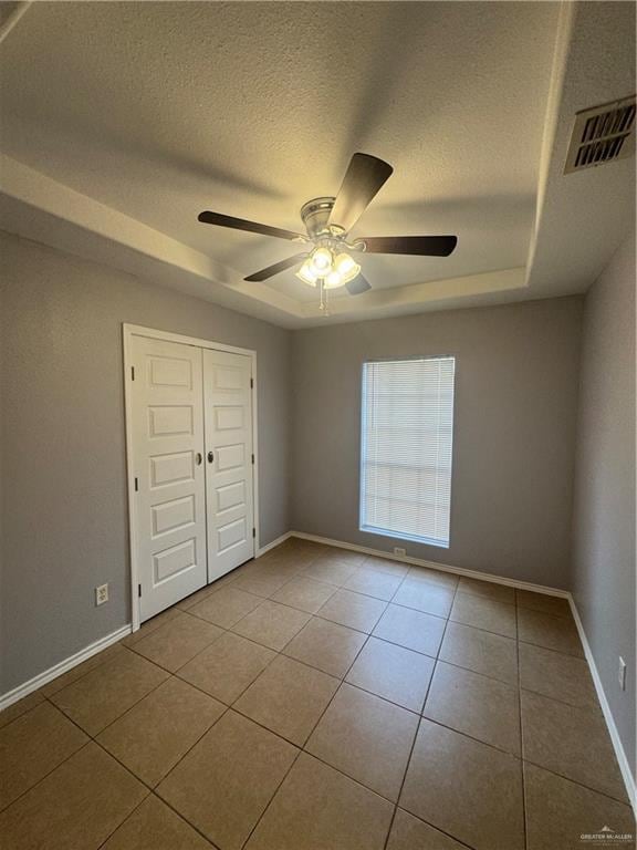 914 Denver St, Edinburg, TX 78541 - unfurnished bedroom featuring tile patterned flooring, a tray ceiling, a textured ceiling, a closet, and ceiling fan