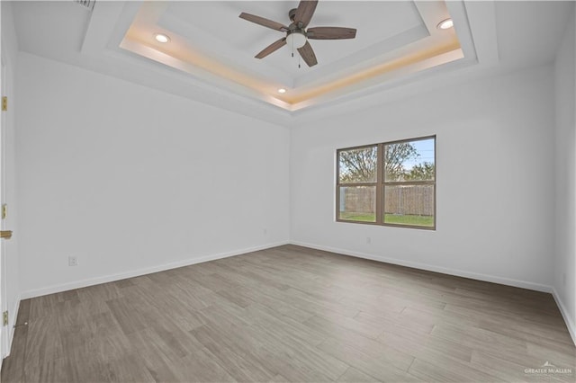 spare room featuring a tray ceiling, ceiling fan, and light hardwood / wood-style floors