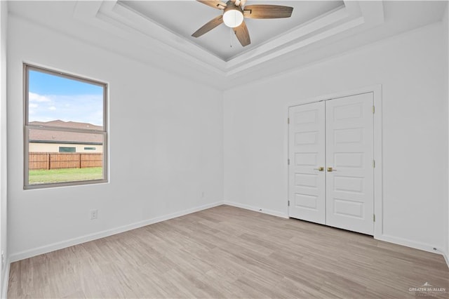 unfurnished room with ceiling fan, light hardwood / wood-style floors, and a raised ceiling