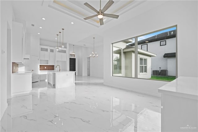 unfurnished living room featuring ceiling fan with notable chandelier, a tray ceiling, and sink