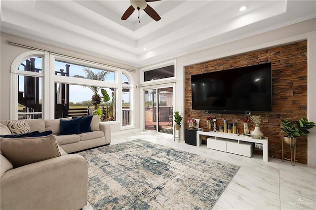 living area with marble finish floor, a raised ceiling, and a ceiling fan