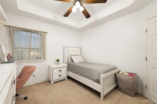 bedroom with ceiling fan, a tray ceiling, baseboards, and light carpet