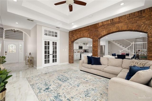 living room featuring visible vents, a ceiling fan, arched walkways, a raised ceiling, and stairs