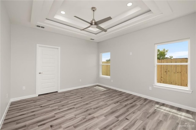 empty room with a ceiling fan, a raised ceiling, plenty of natural light, and visible vents