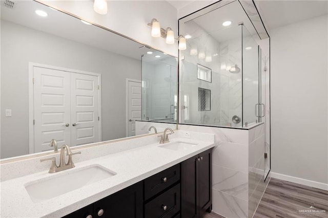 bathroom with a shower stall, double vanity, wood finished floors, and a sink
