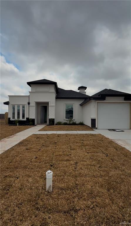 prairie-style home with a front yard, concrete driveway, stucco siding, and an attached garage