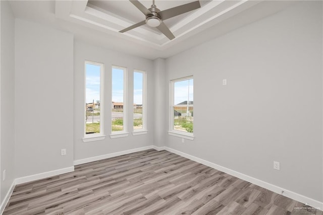 empty room featuring a tray ceiling, baseboards, wood finished floors, and ceiling fan