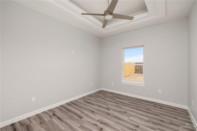 unfurnished room featuring a tray ceiling, baseboards, wood finished floors, and a ceiling fan