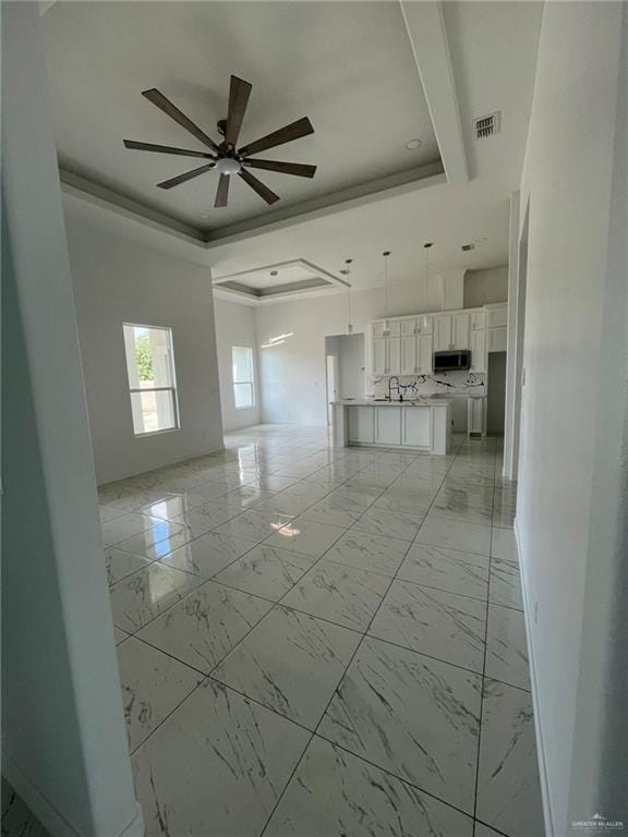 411 Thornwood Loop, Rio Grande City, TX 78582 - unfurnished living room with a tray ceiling, a ceiling fan, a sink, baseboards, and light marble finish flooring