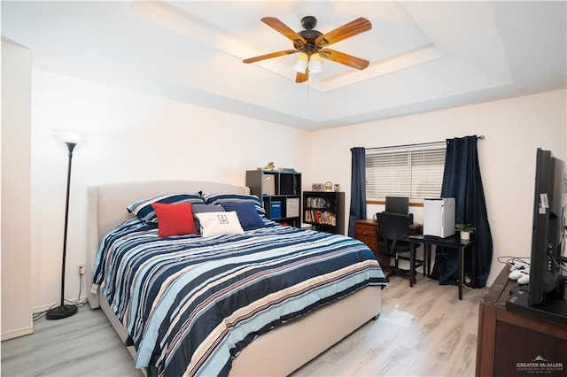 bedroom featuring ceiling fan, a raised ceiling, and light wood-type flooring