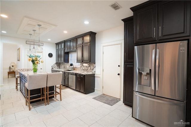 kitchen featuring light tile patterned flooring, a breakfast bar area, decorative light fixtures, stainless steel appliances, and backsplash