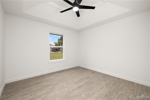 empty room with ceiling fan, a raised ceiling, and light hardwood / wood-style flooring