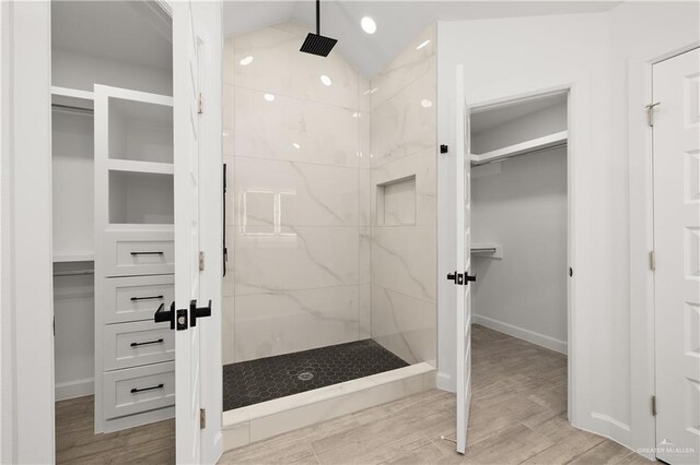 bathroom with hardwood / wood-style floors, tiled shower, and vaulted ceiling