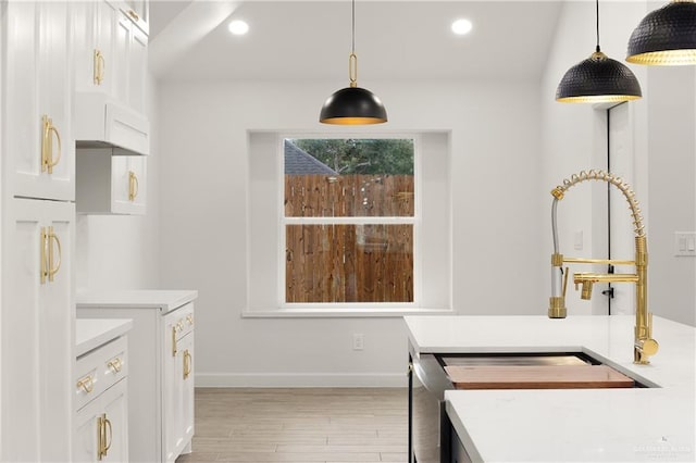 kitchen featuring white cabinets, light wood-type flooring, hanging light fixtures, and sink