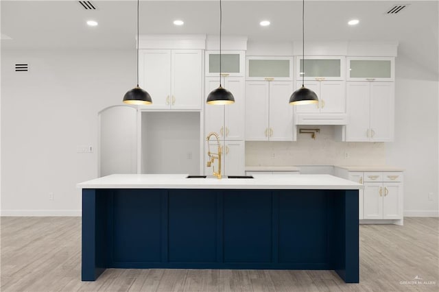 kitchen with sink, an island with sink, light hardwood / wood-style floors, and decorative light fixtures