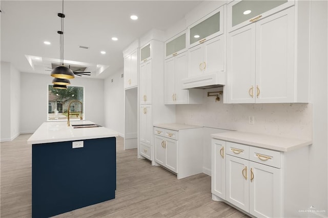 kitchen with white cabinetry, sink, light hardwood / wood-style floors, decorative light fixtures, and a center island with sink