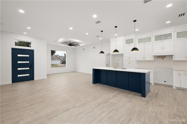 kitchen featuring ceiling fan, sink, light hardwood / wood-style floors, decorative light fixtures, and a center island with sink