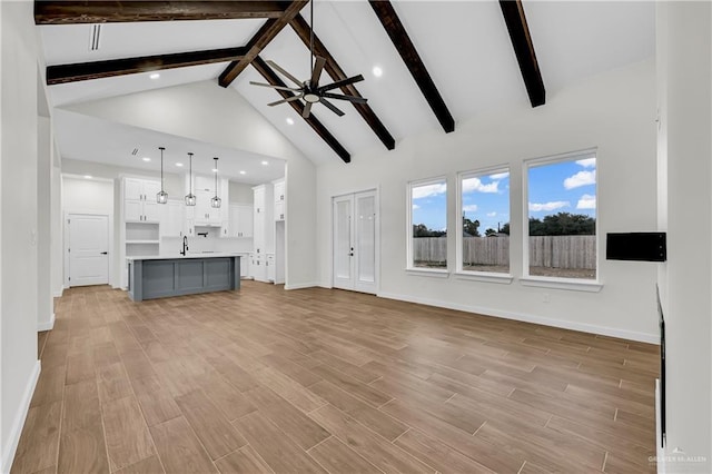 unfurnished living room featuring sink, beam ceiling, high vaulted ceiling, and ceiling fan