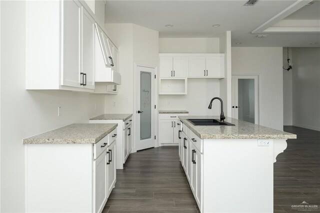 kitchen featuring light stone counters, dark wood finished floors, a center island with sink, white cabinetry, and a sink