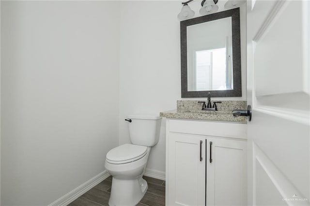 half bath featuring wood tiled floor, baseboards, vanity, and toilet