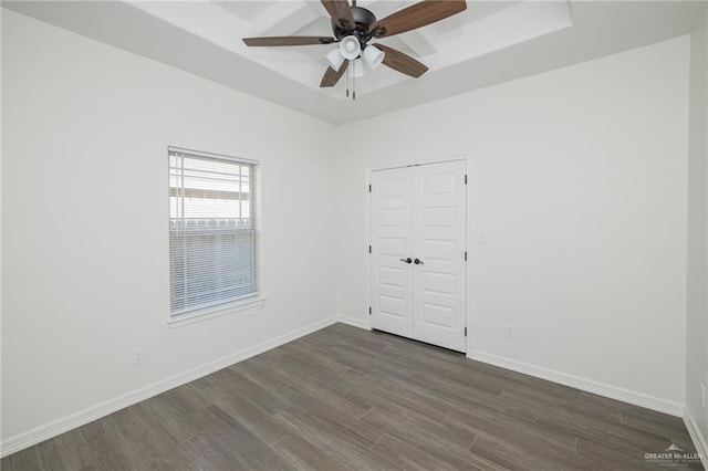 empty room featuring ceiling fan, baseboards, a raised ceiling, and dark wood finished floors