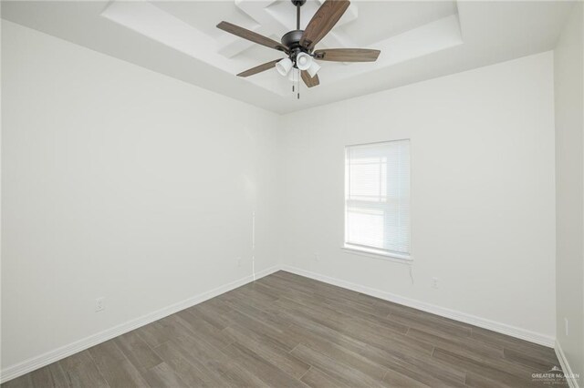 empty room featuring dark wood-style flooring, a raised ceiling, a ceiling fan, and baseboards