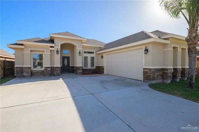 prairie-style home with an attached garage, fence, stone siding, driveway, and stucco siding