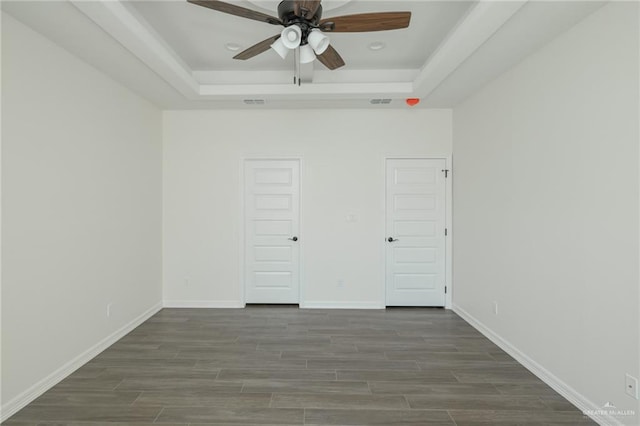 unfurnished bedroom with ceiling fan, wood finished floors, a raised ceiling, and baseboards