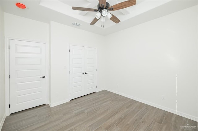 unfurnished bedroom with wood finished floors, a raised ceiling, visible vents, and baseboards