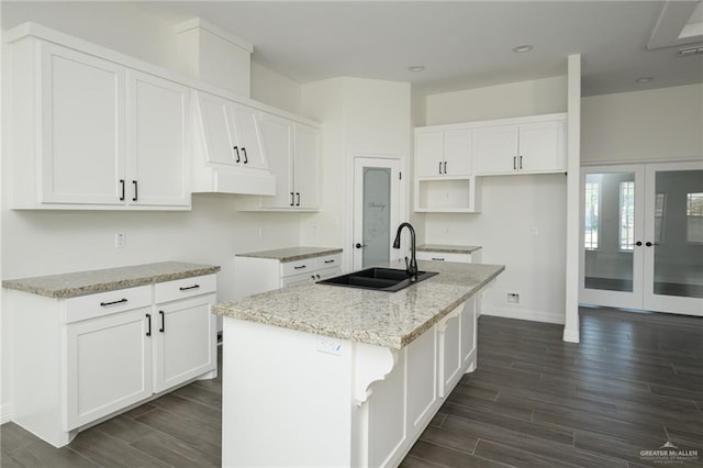 kitchen featuring light stone counters, wood finish floors, a kitchen island with sink, and a sink