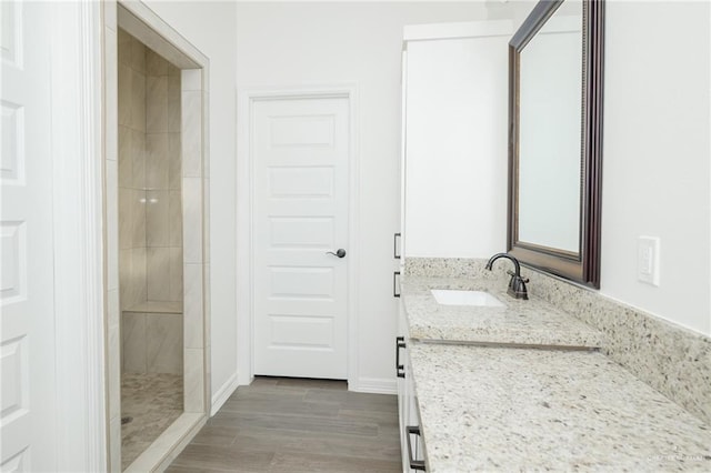 bathroom with a tile shower, vanity, baseboards, and wood finished floors