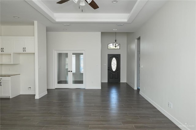 foyer with dark wood-style floors, a raised ceiling, french doors, and ceiling fan with notable chandelier