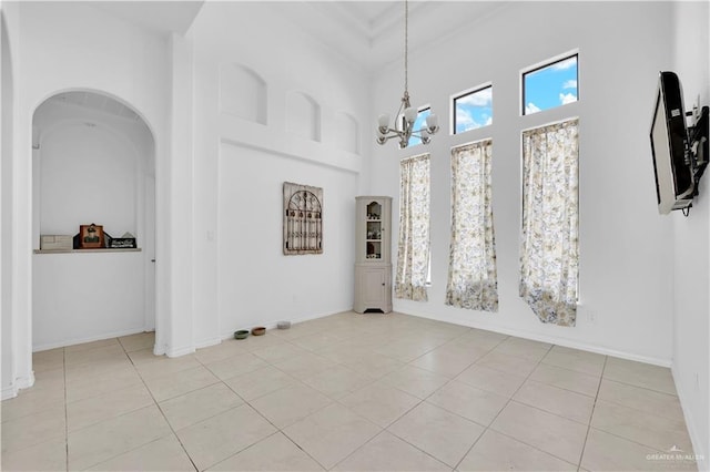 unfurnished dining area with baseboards, a notable chandelier, light tile patterned flooring, and a towering ceiling