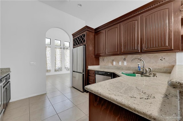 kitchen featuring tasteful backsplash, light stone countertops, stainless steel appliances, and a sink