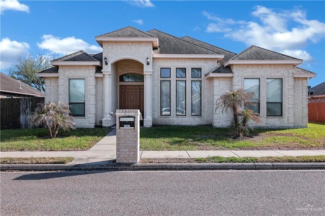 view of front of house featuring brick siding, roof with shingles, a front yard, and fence