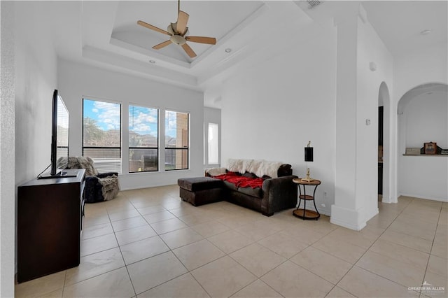 living room with light tile patterned floors, a ceiling fan, a tray ceiling, arched walkways, and a towering ceiling