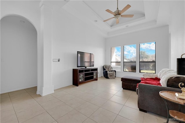 living room featuring ceiling fan, baseboards, a tray ceiling, light tile patterned floors, and arched walkways