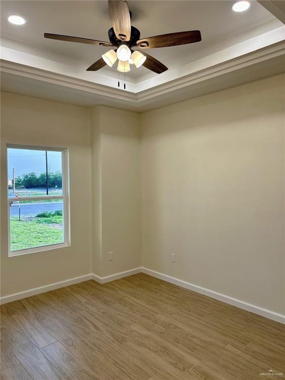 empty room featuring light wood finished floors, recessed lighting, baseboards, and a tray ceiling
