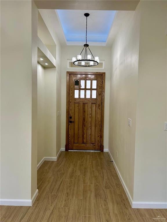 doorway to outside featuring light wood finished floors, baseboards, a tray ceiling, and a notable chandelier